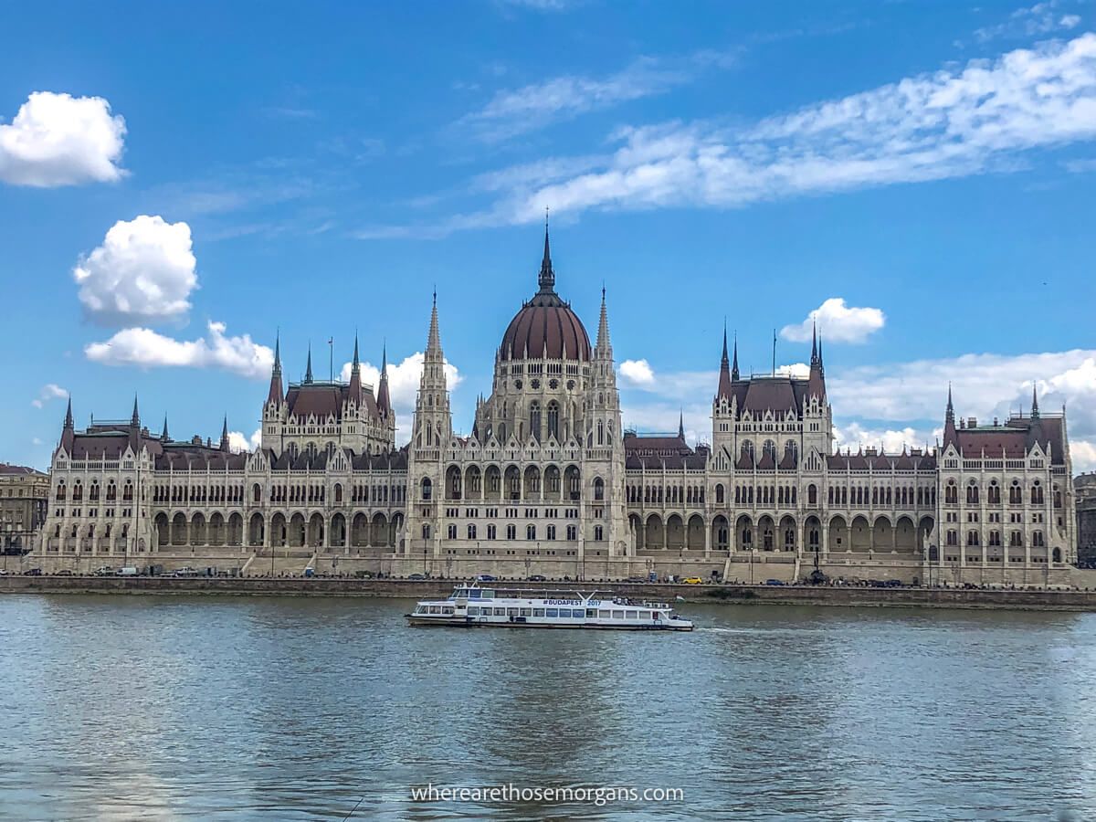 River with a cruise boat passing by the Hungarian Parliament Building in Budapest on a sunny day with blue sky
