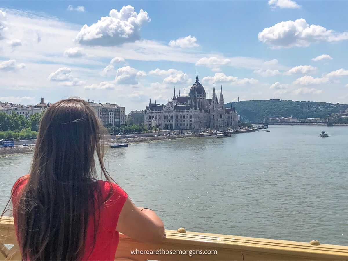 Tourist on a bridge looking at a huge Gothic style building on the banks of a river on a sunny day