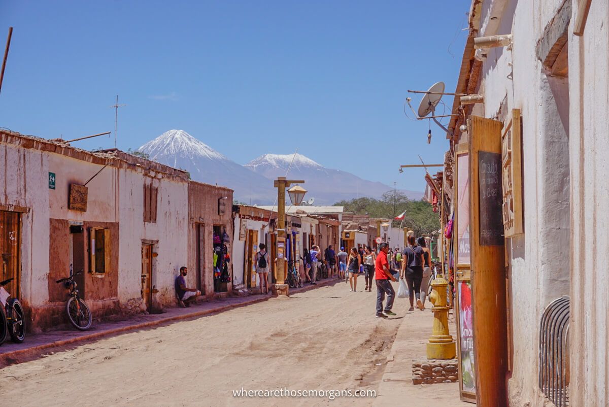 Photo of a dusty street in San Pedro de Atacama with white painted concrete buildings flanking and people walking