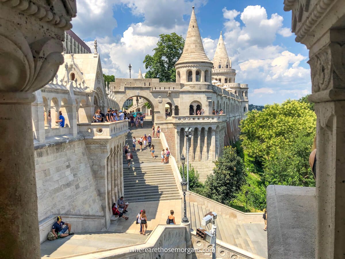 Photo of a stone fortress taken through a window with a staircase leading to walls with turrets on a sunny day with light clouds