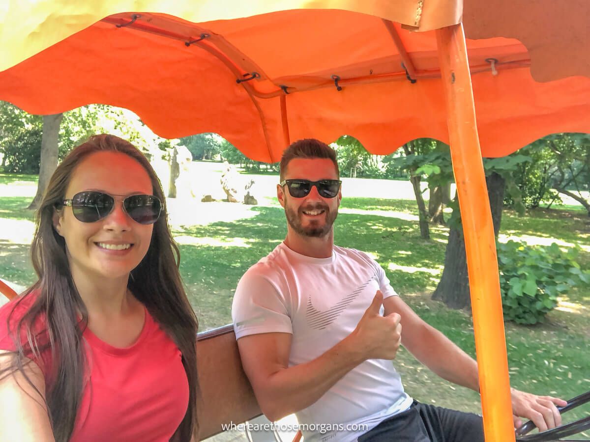 Photo of a couple riding through a park in Budapest in a quad bicycle with an orange canopy
