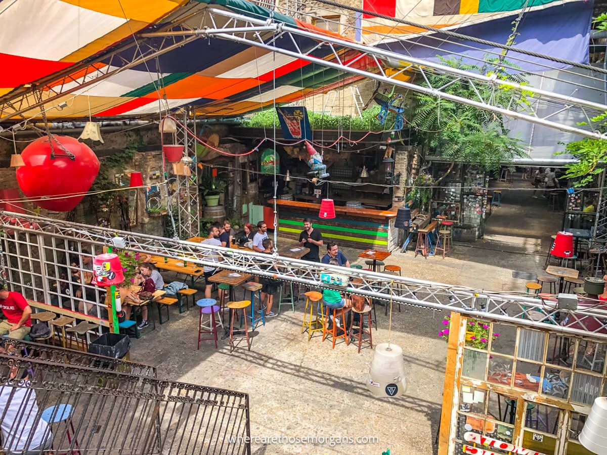 Photo looking down over an open courtyard with people sat at tables and chairs, and a roof made of flags