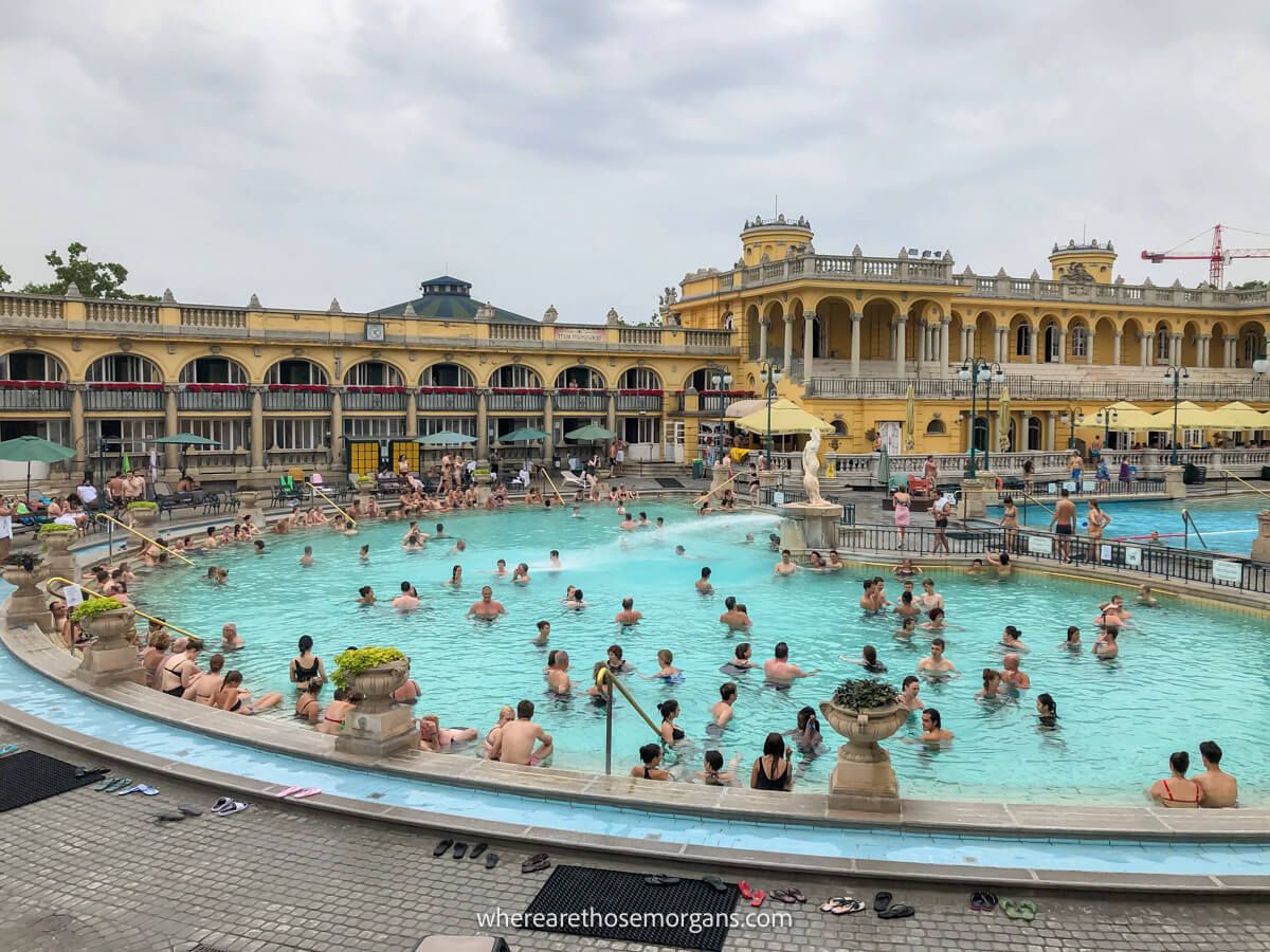 Photo of an outdoor thermal pool with lots of tourists bathing under a. cloudy sky