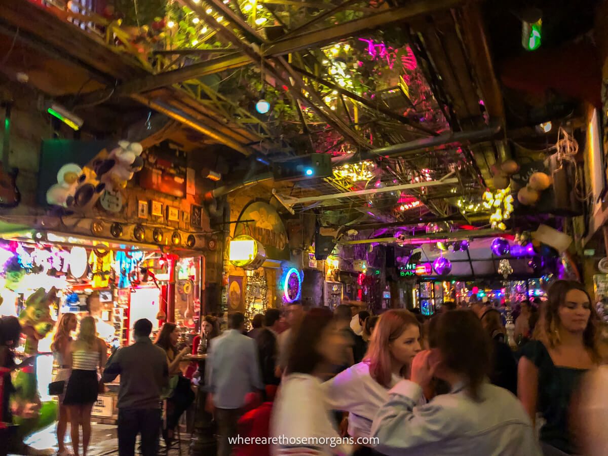 Inside a bustling ruin bar in Budapest at night with lots of tourists drinking beers and dancing with lights flashing and lots of colorful exhibits