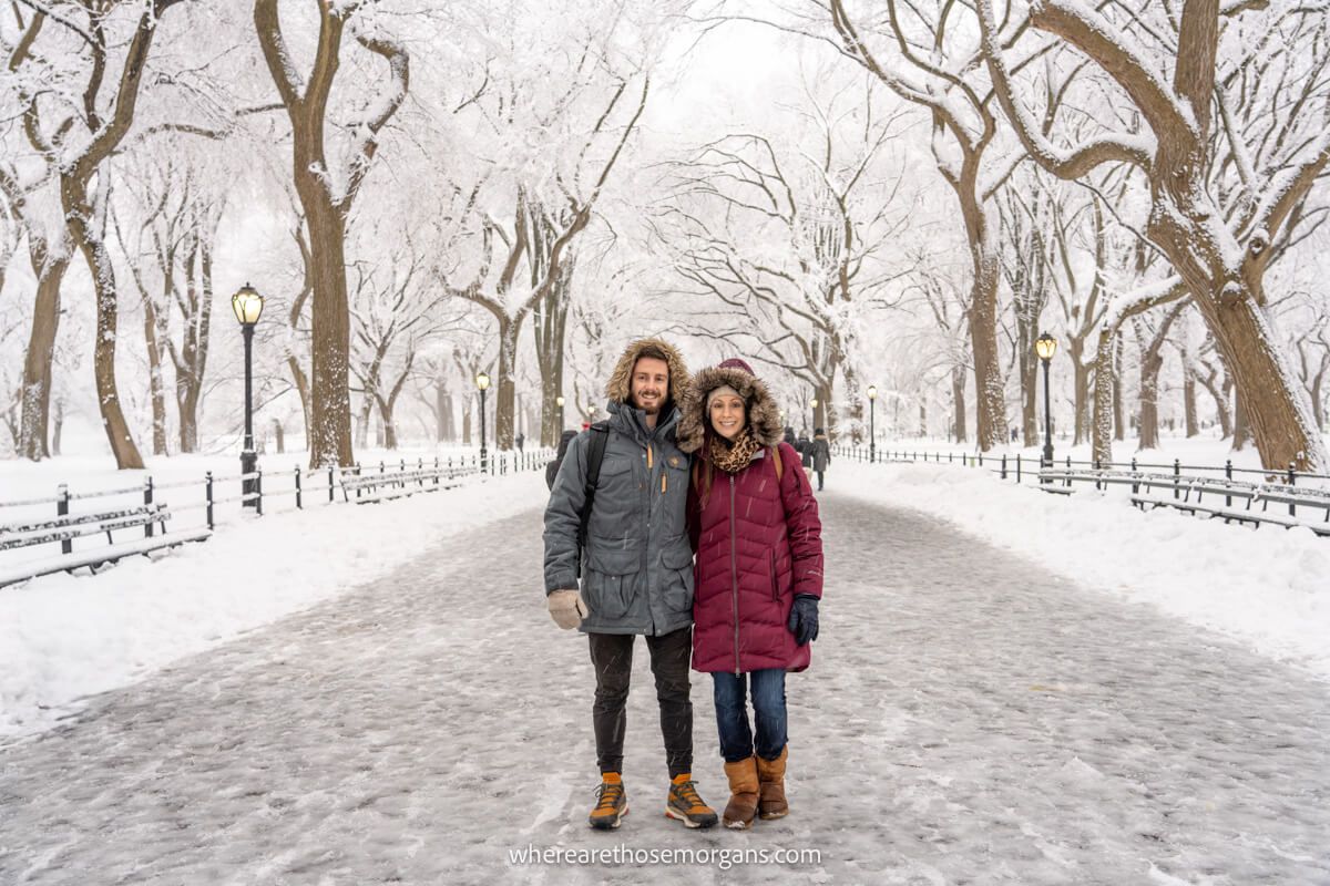 Photo of a couple standing together for a photo on an empty path surrounded by snow and bare trees