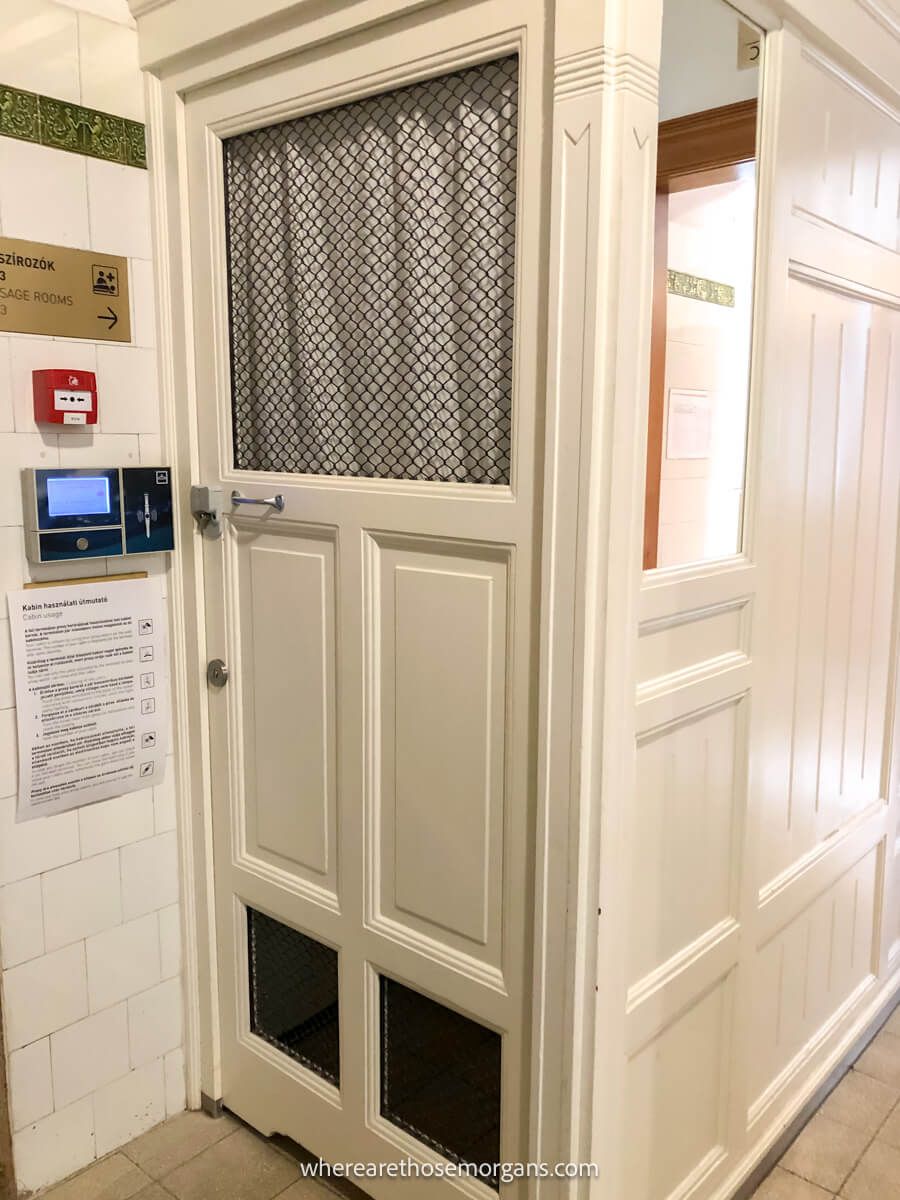 Narrow changing cubicle with a white door and secure entry inside a thermal baths