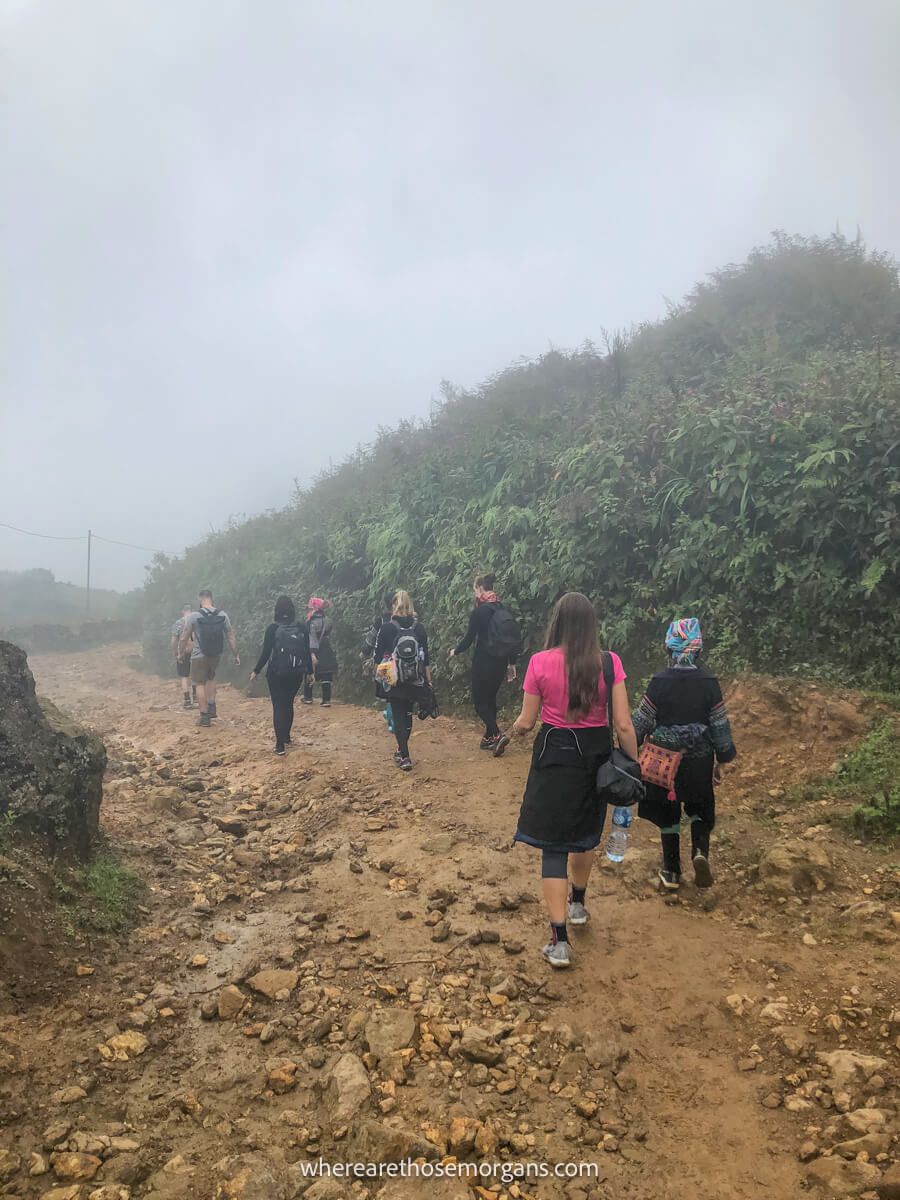 Several people hiking down a dirt path in the fog and rain