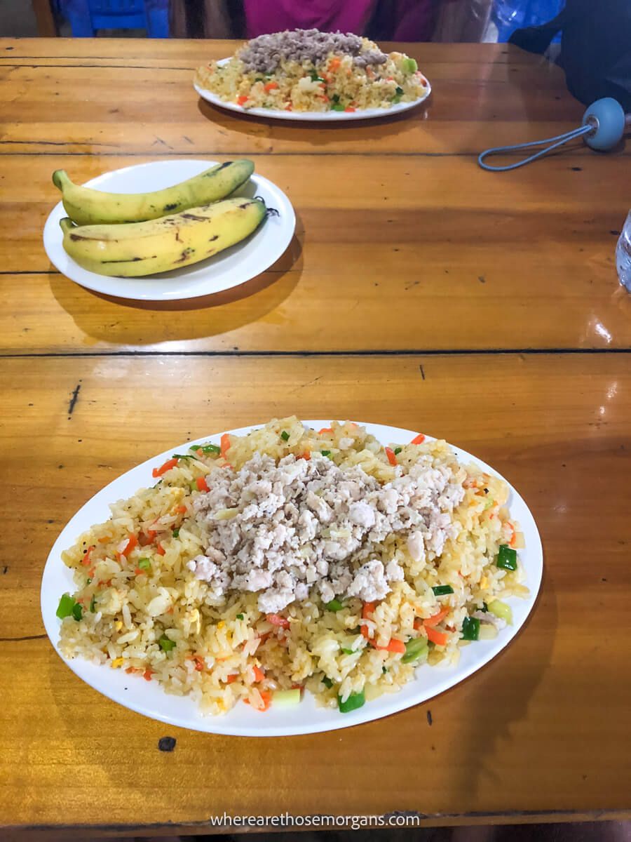 Two bananas on a plate along with two plates of fried rice
