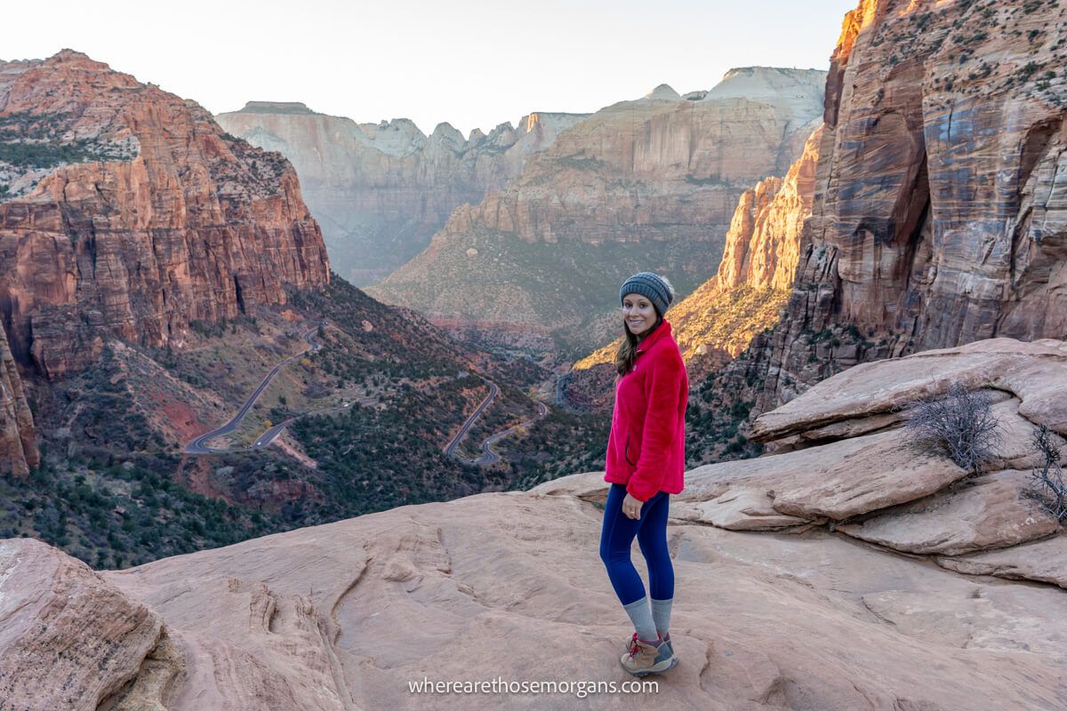 Photo of a hiker standing on a rocky summit ledge with views over a deep canyon and tall cliff walls at sunset