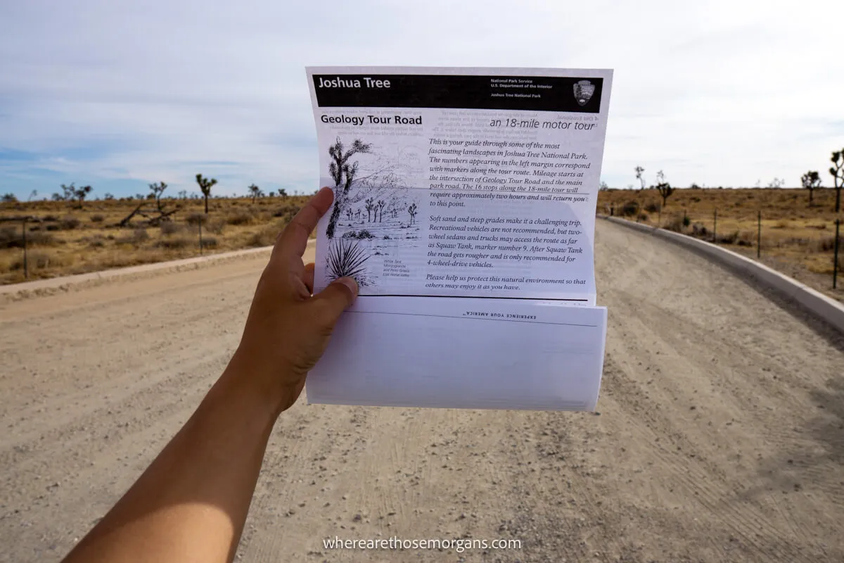 Photo of a tourist holding out an arm with a piece of paper listing driving instructions for a 4WD road in a desert