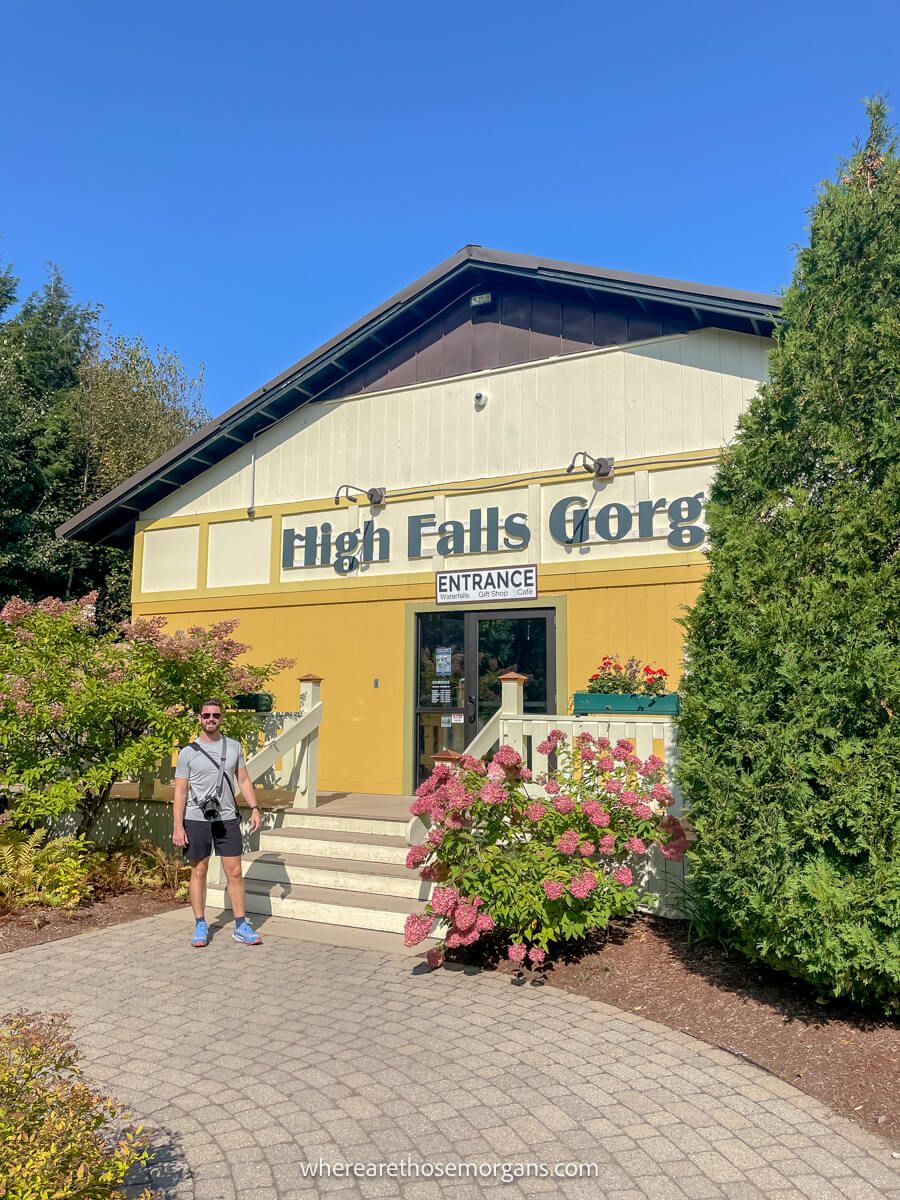 Photo of a tourist at the entrance to a building painted yellow next to tall evergreen trees on a sunny day