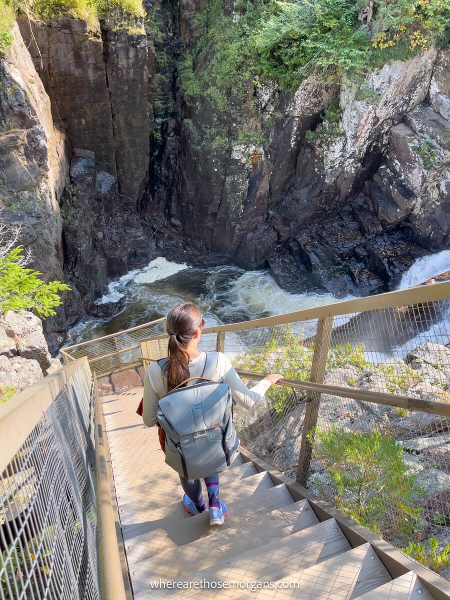 Photo of a hiker walking down a steep metal staircase into a gorge with a river running through
