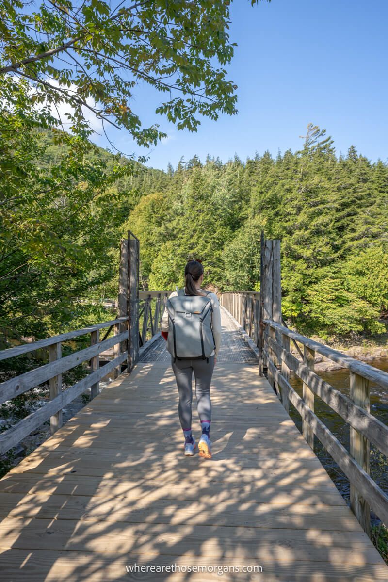 Photo of a hiker crossing a wooden bridge towards a forest on a sunny day