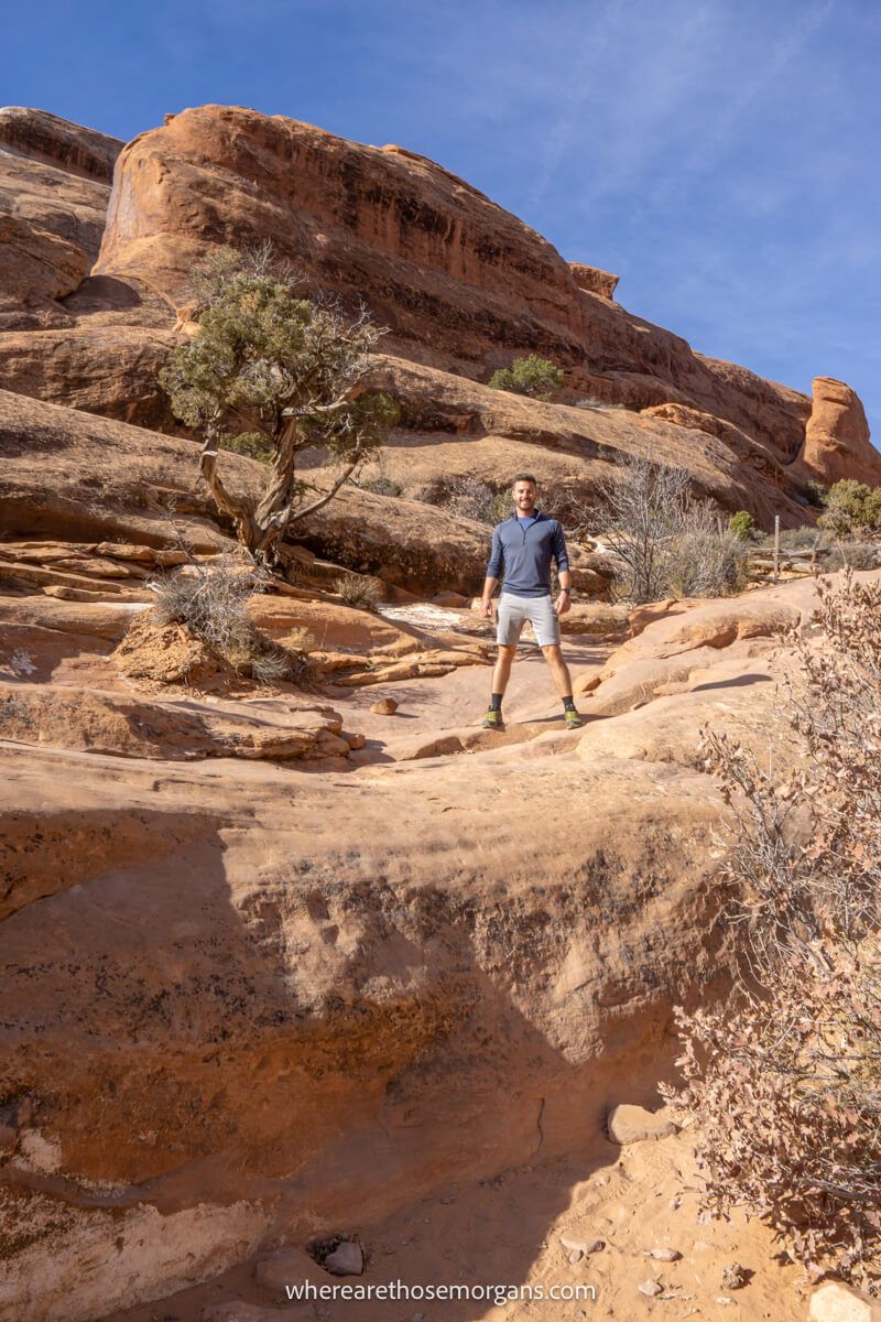 Photo of a hiker walking on a red rock trail in a desert landscape