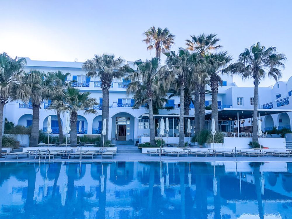 A hotel with a pool and palm trees in Greece