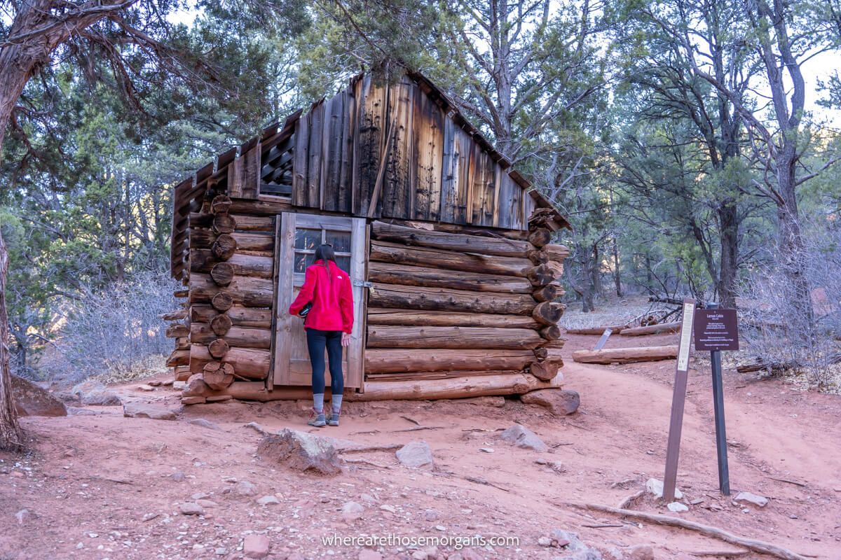 Photo of a hiker looking into a door of a log cabin in a forest in Utah