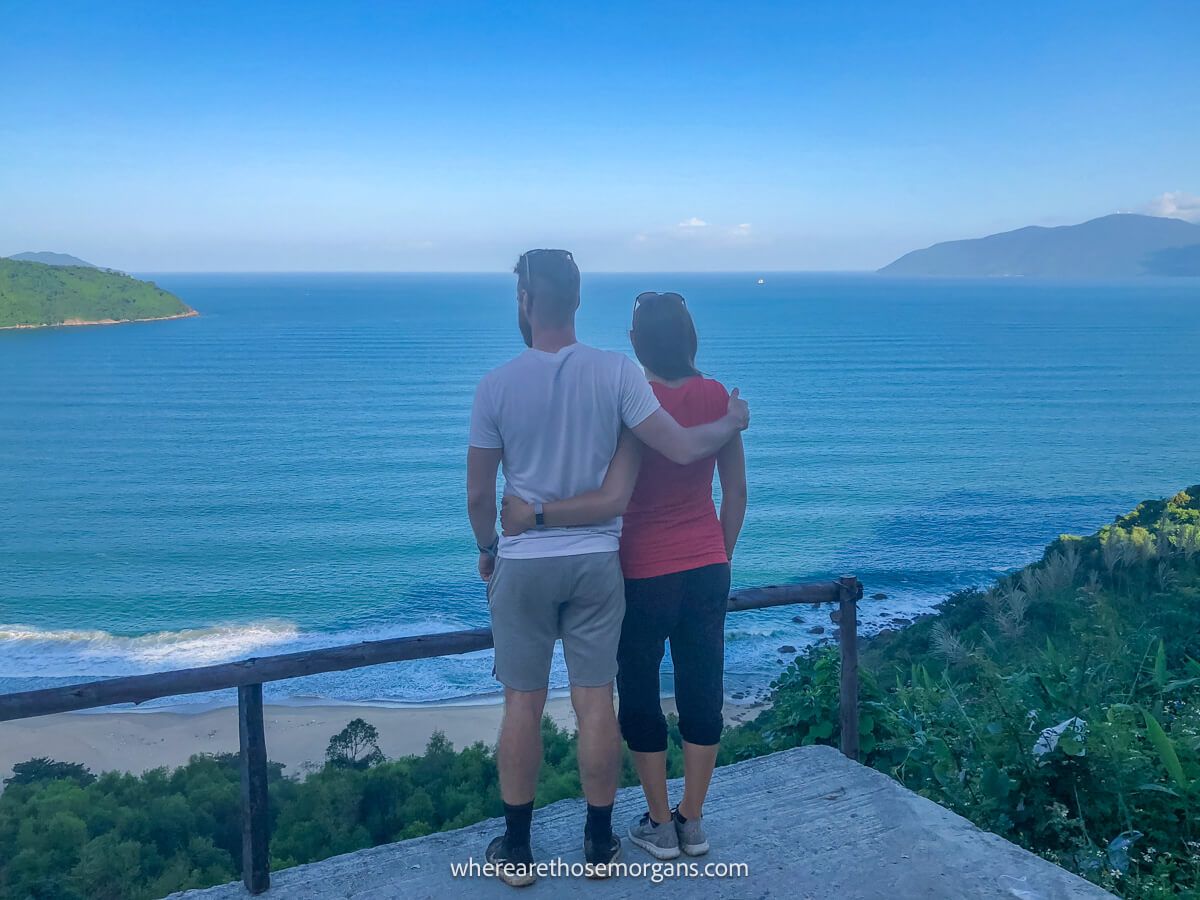Man and woman embracing for a photo as they look out over the beautiful ocean with waves crashing on the beach