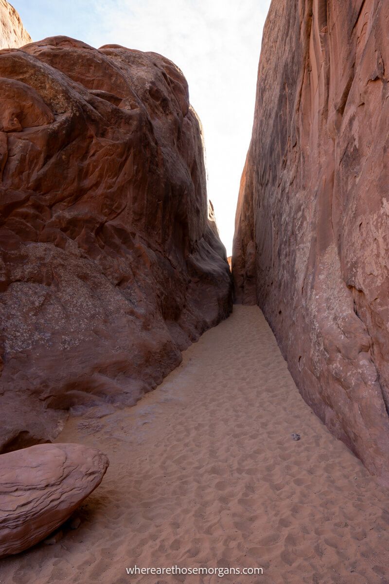 Photo of a sandy trail leading through narrow red rocks