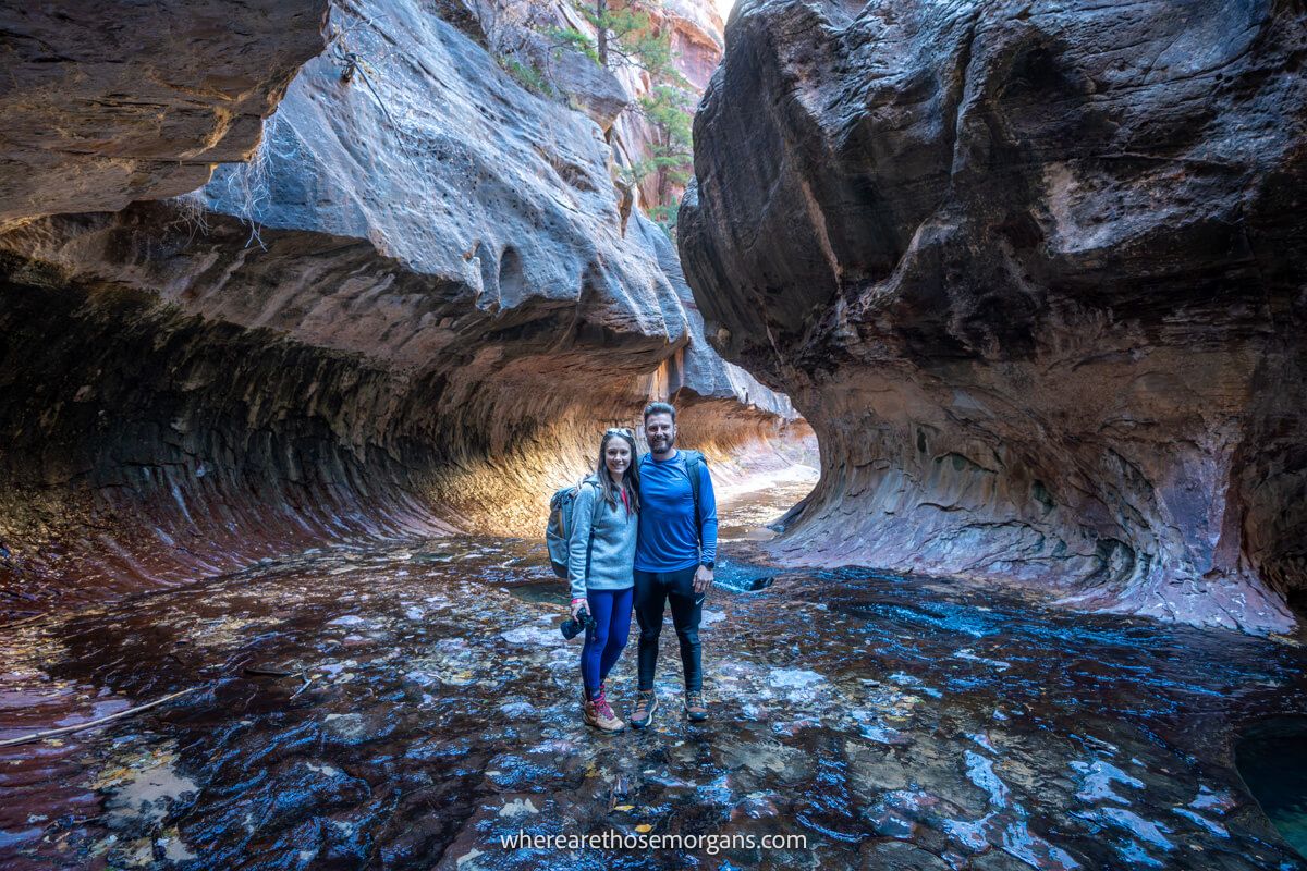Photo of a couple standing together inside a natural tunnel-like rock formation called The Subway in Zion