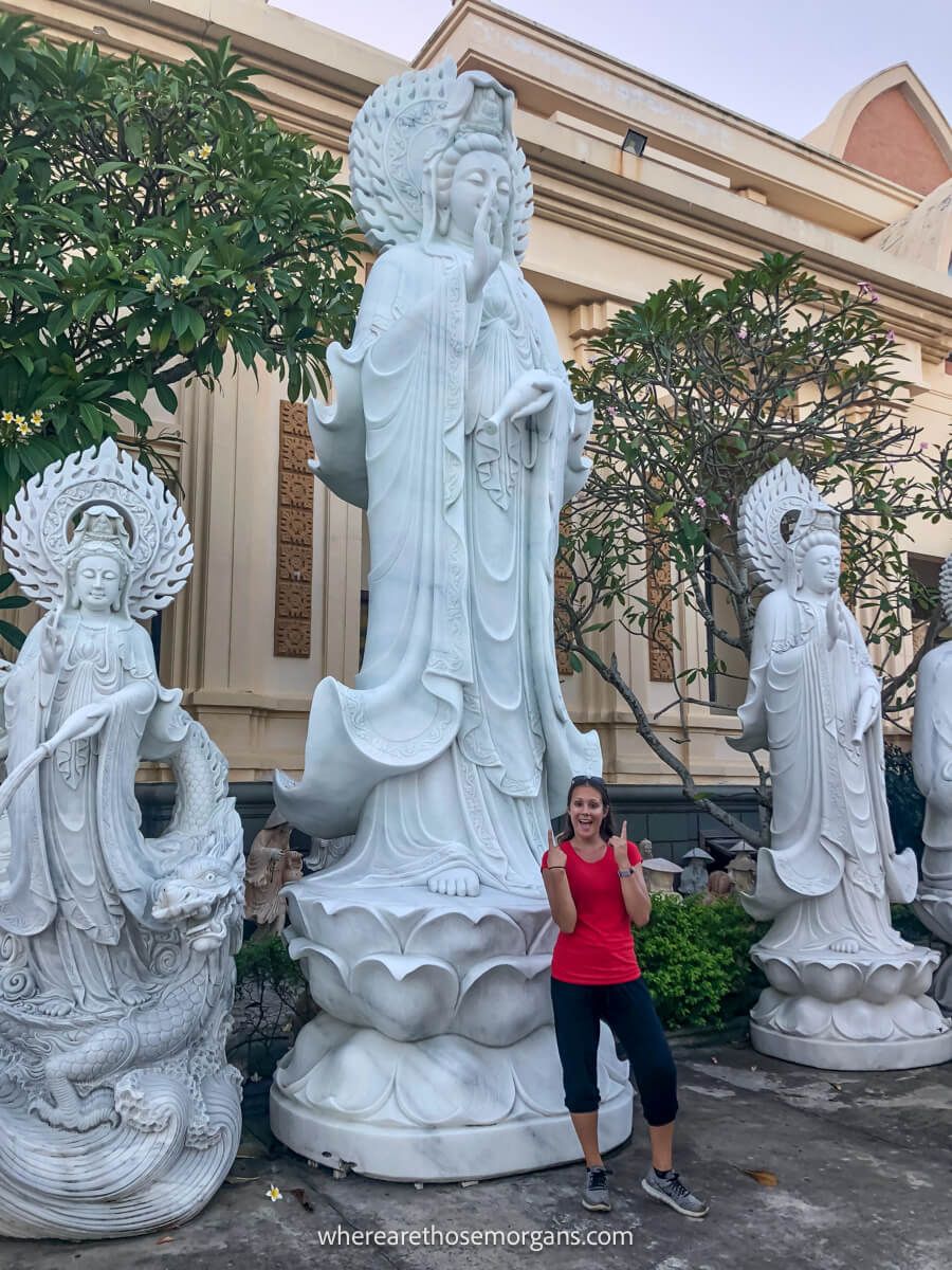 Woman in a red shirt pointing to a large white statue made from marble