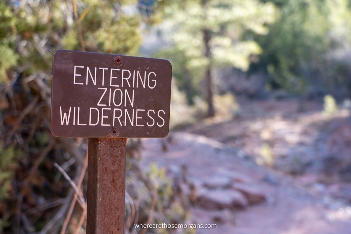 Photo of a small brown sign on a hiking trail stating entering Zion wilderness