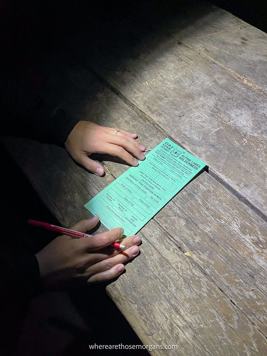 Photo of hands with a pen filling in a permit on a wooden bench lit by headlamp light