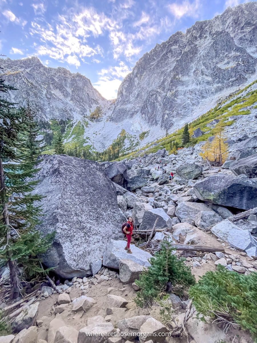 Photo of a hiker walking through a boulder field towards Aasgard Pass in Washington under a blue sky at dawn