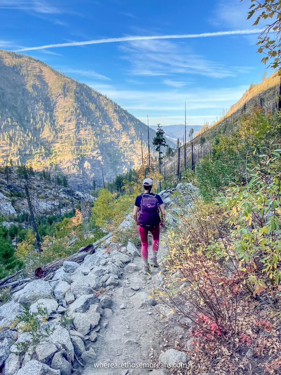 Photo of a person walking along a narrow path on a hillside in between mountains on a sunny day