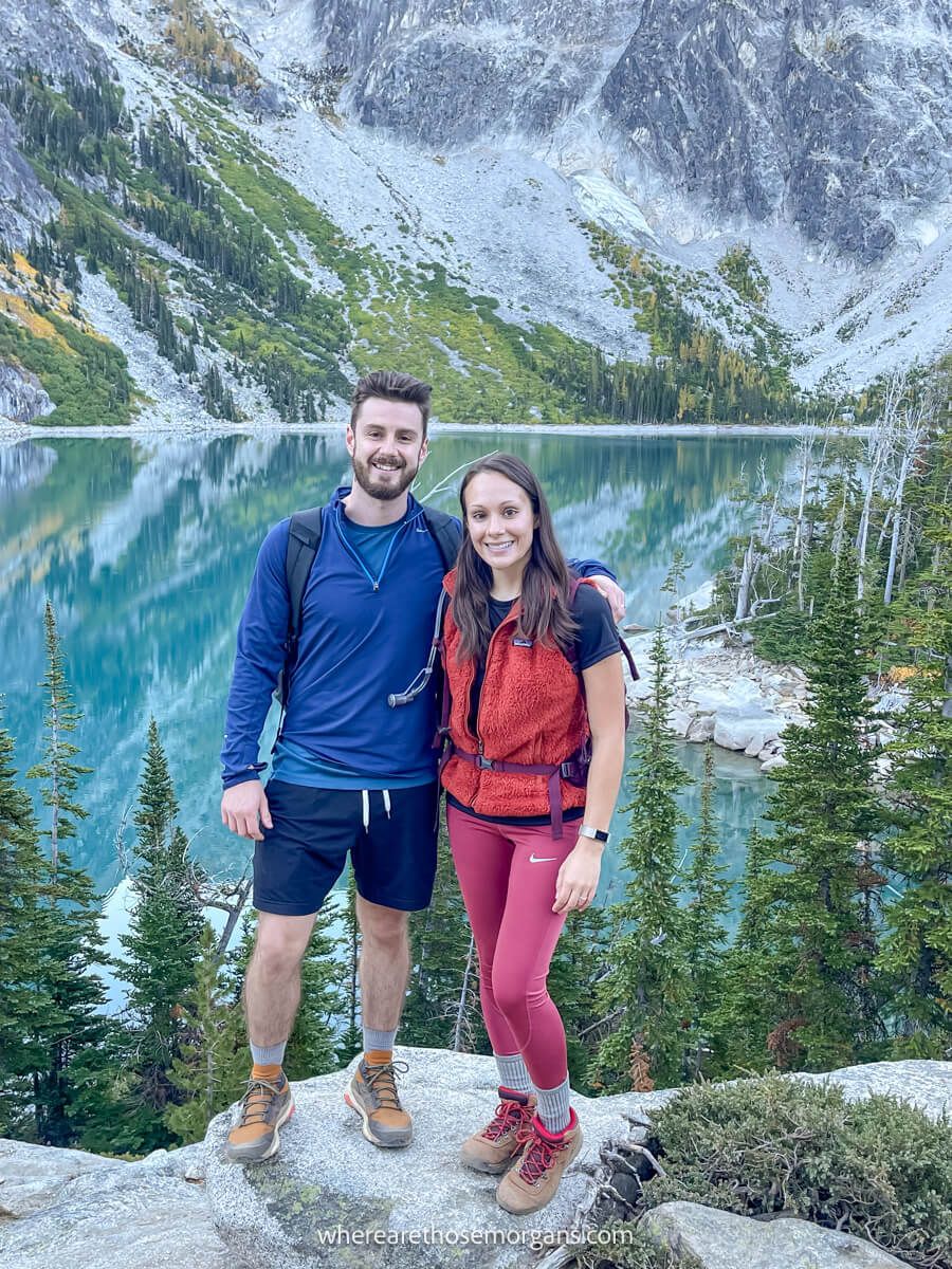 Photo of Mark and Kristen Morgan from Where Are Those Morgans hiking The Enchantments Trail standing on a rock with a lake in the background