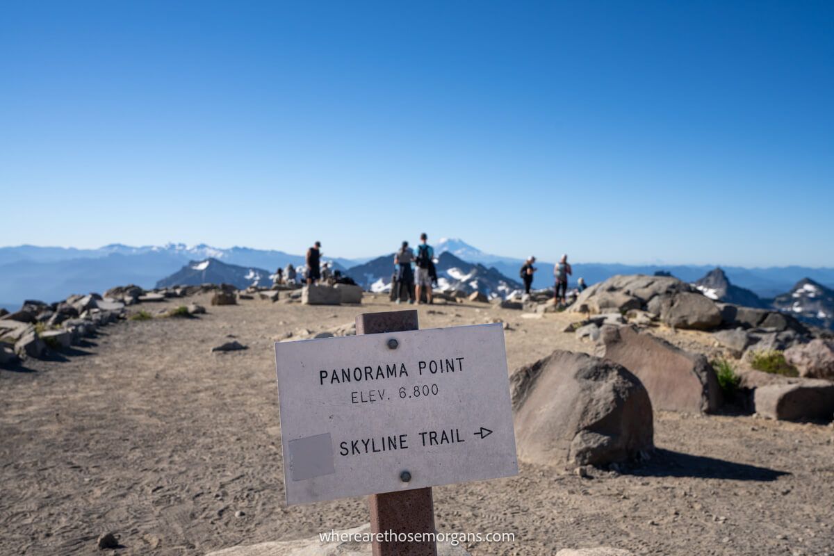 Photo of a trail sign reading Panorama Point with a few hikers at a vista overlooking distant mountain views