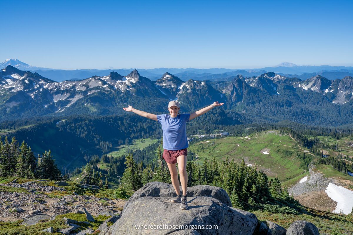 Photo of Kristen Morgan from Where Are Those Morgans holding arms out on a rock with views over mountains on a sunny day hiking Skyline Trail in Mount Rainier National Park
