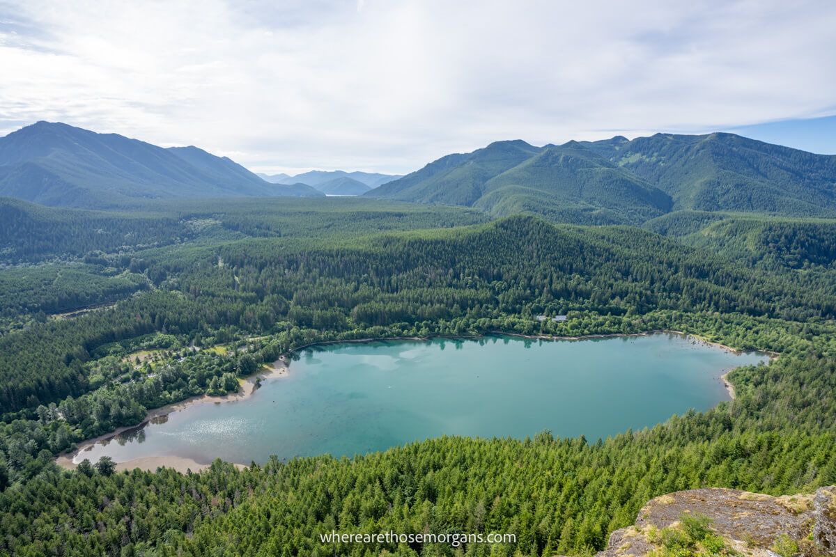 Photo of a blue lake surrounded by trees and rolling hills under a cloudy sky