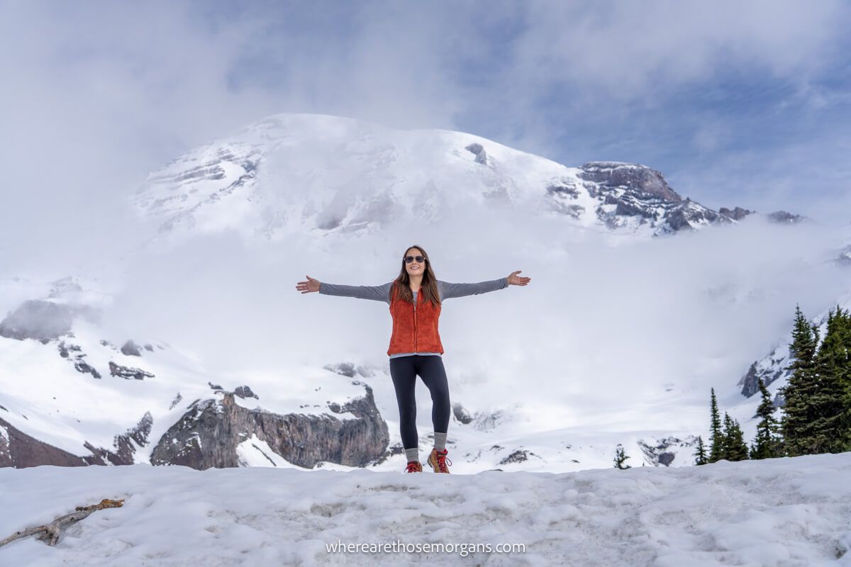 Photo of Kristen Morgan from Where Are Those Morgans standing alone on a snowy path with Mt Rainier behind on the Skyline Trail in June