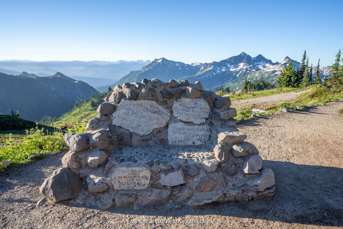 Photo of a rock bench on a path half way up a mountain with far reaching views behind under a clear sky
