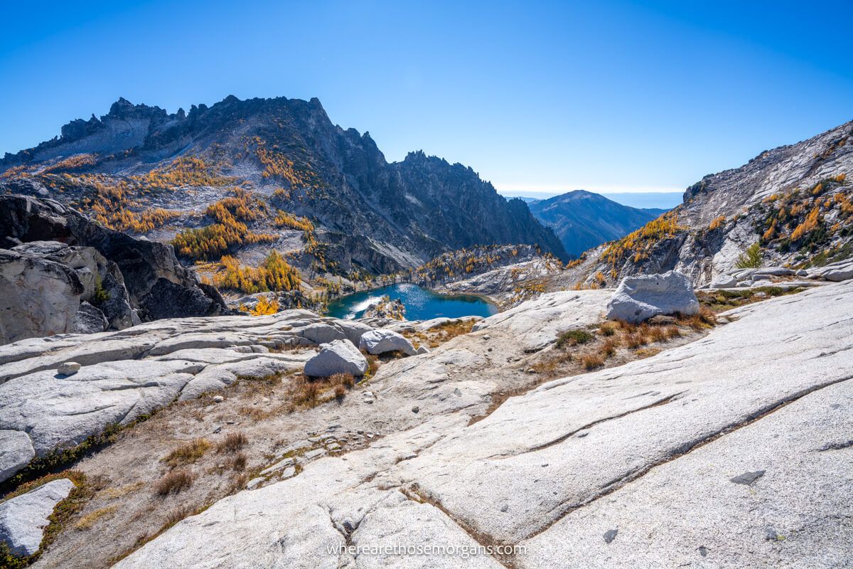 Photo of a small blue lake and golden larch trees in a granite rock landscape under a blue sky at The Core Enchantments in Washington