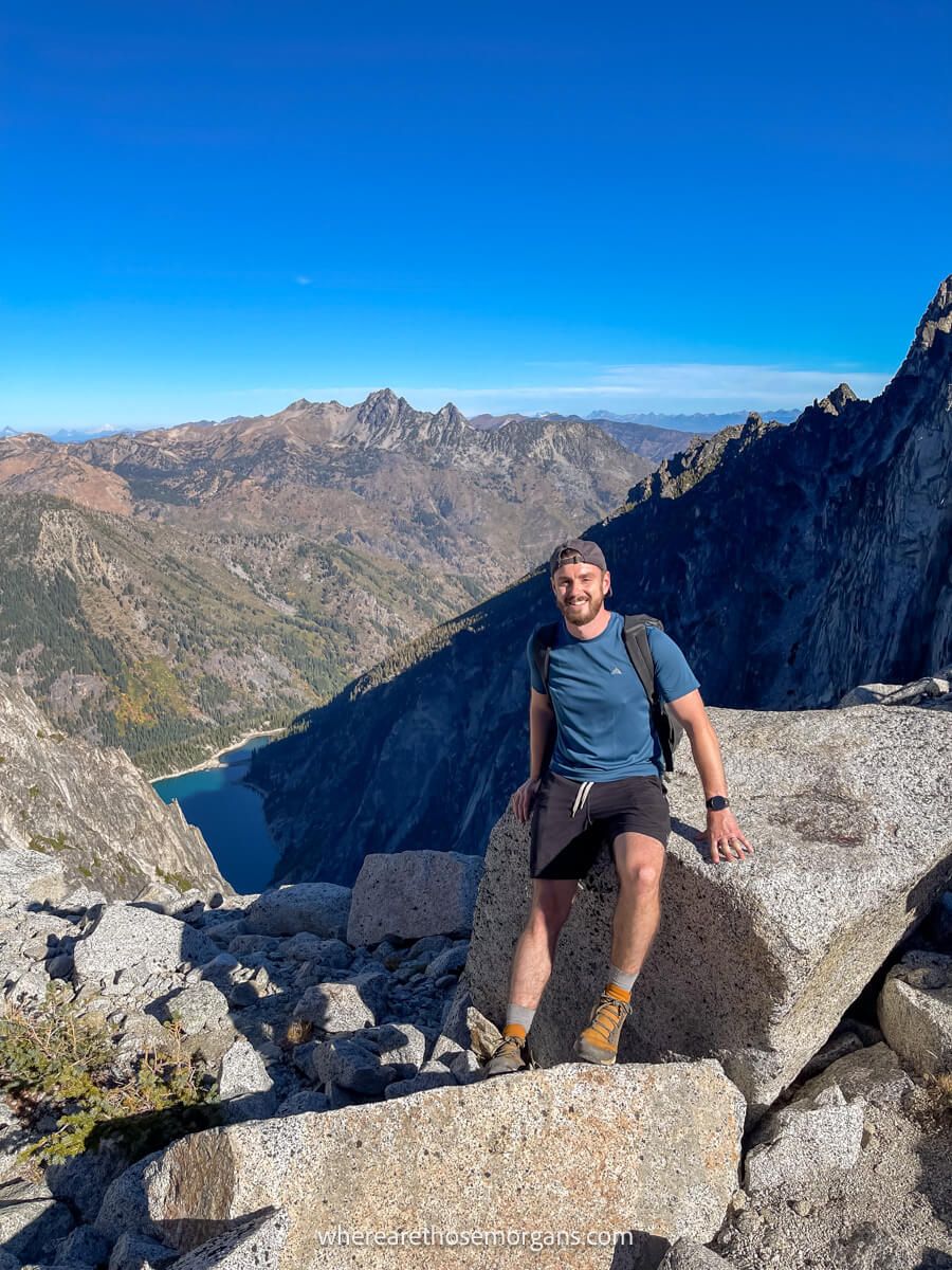 Photo of a hiker sat on a boulder at the top of a mountain pass under a clear blue sky