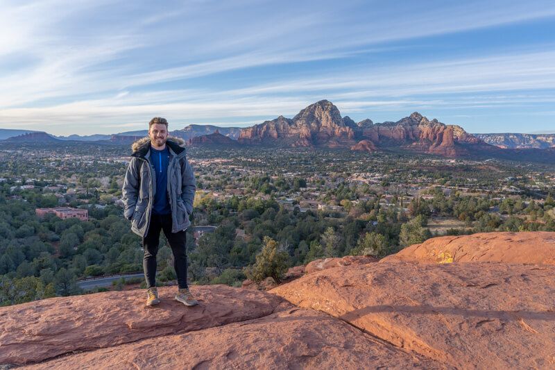 Photo of Mark Morgan in a winter coat standing on a flat red rock formation with wide open views behind