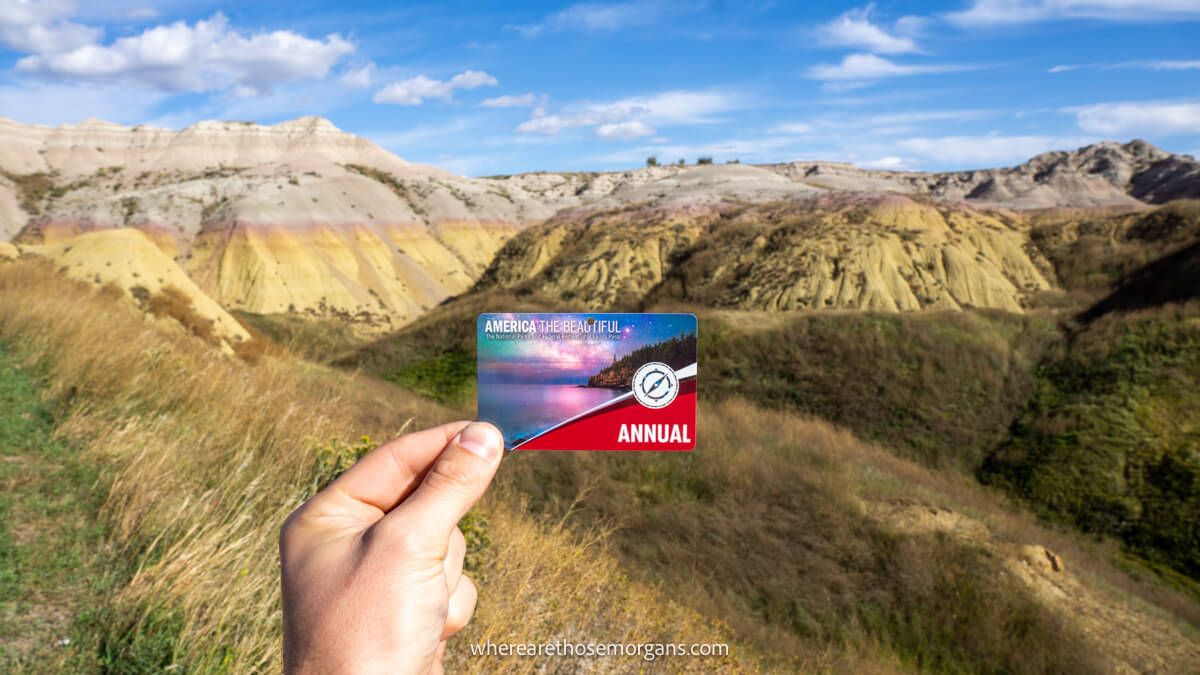 Photo of a hand holding a national park pass in front of yellow mounds in the Badlands, South Dakota