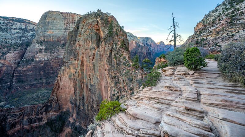 Photo of a narrow rocky hiking path leading to a shark fin shaped rock formation in a striking canyon at dawn