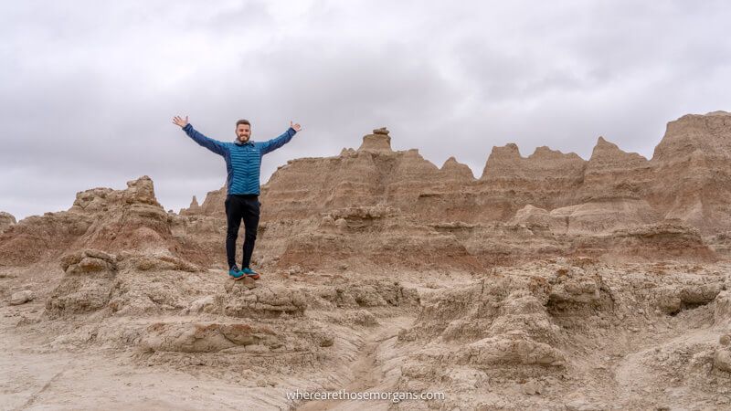 Photo of a hiker standing on rugged rocks with arms in the air at Badlands National Park on a cloudy day