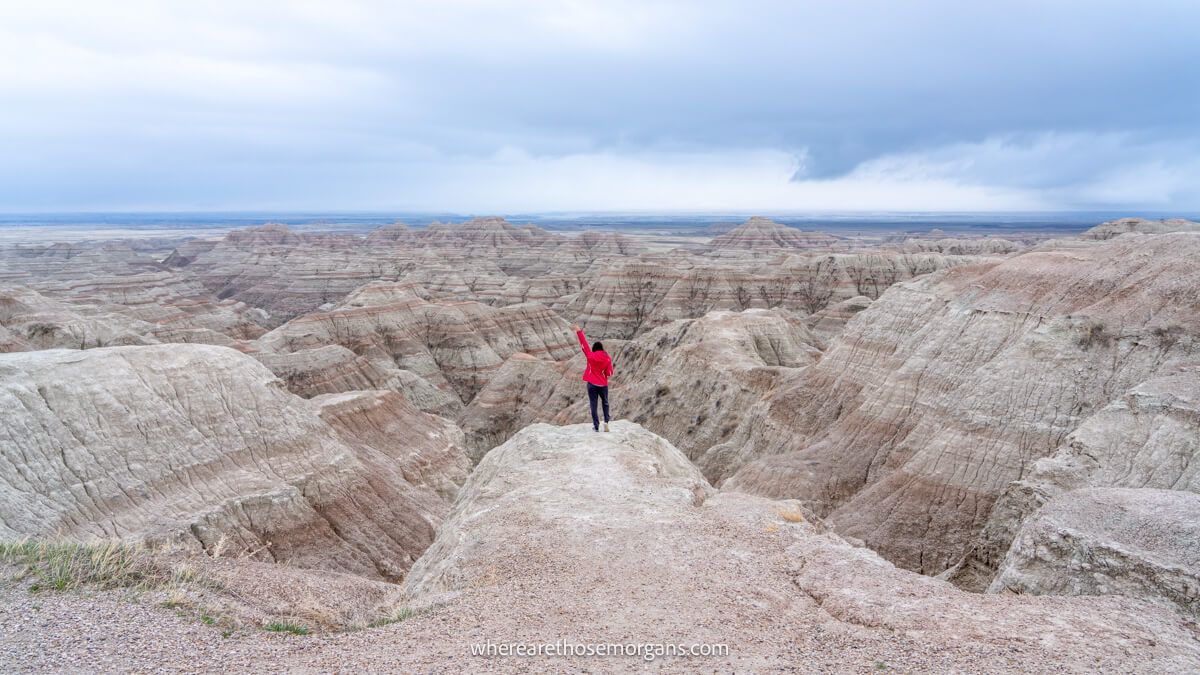 Photo of a hiker in the distance stood on a rocky ledge overlooking the Badlands in South Dakota under a cloudy dark sky
