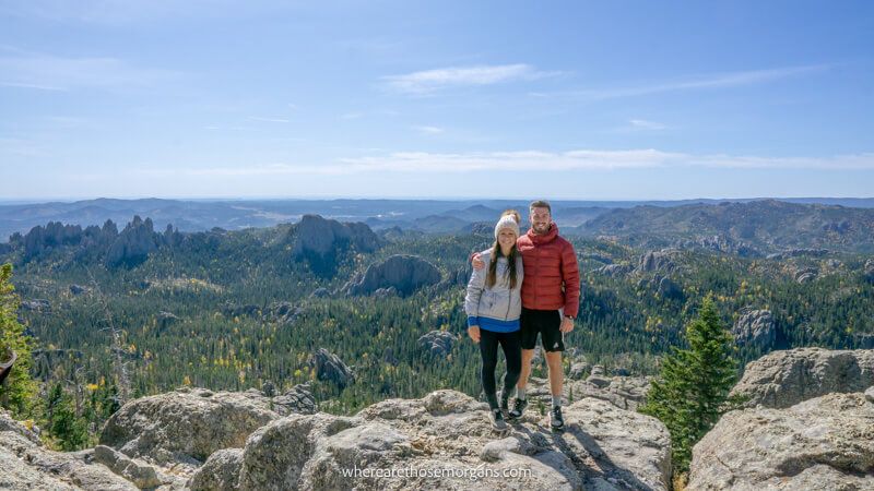 Photo of Mark and Kristen Morgan from Where Are Those Morgans standing together on top of a hiking trail summit with far reaching views over rolling hills covered in trees