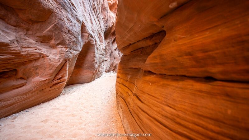 Photo of a narrow sandy path leading through a red rock slot canyon