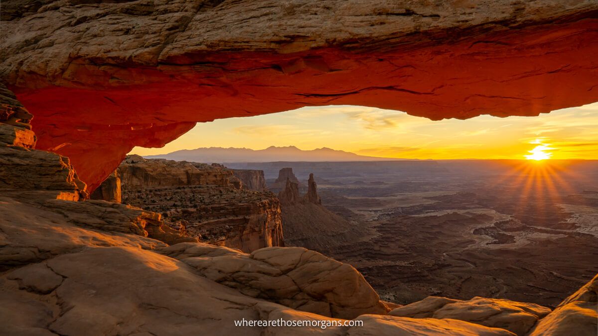 Photo of a natural rock formation shaped like an eye glowing red with views over a desert rocky landscape at sunrise