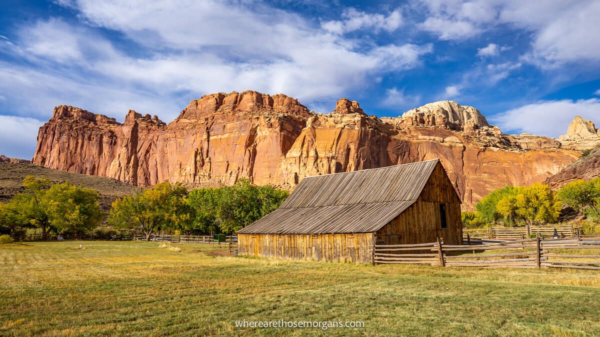 Photo of a grassy field leading to a wooden barn and red rock cliffs on a sunny day