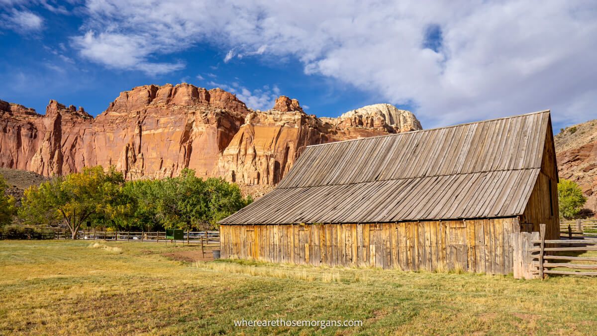A wooden barn in a grassy field with red rocks behind under a blue sky
