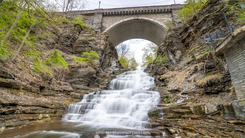 Photo of a waterfall flowing through a gorge underneath a bridge