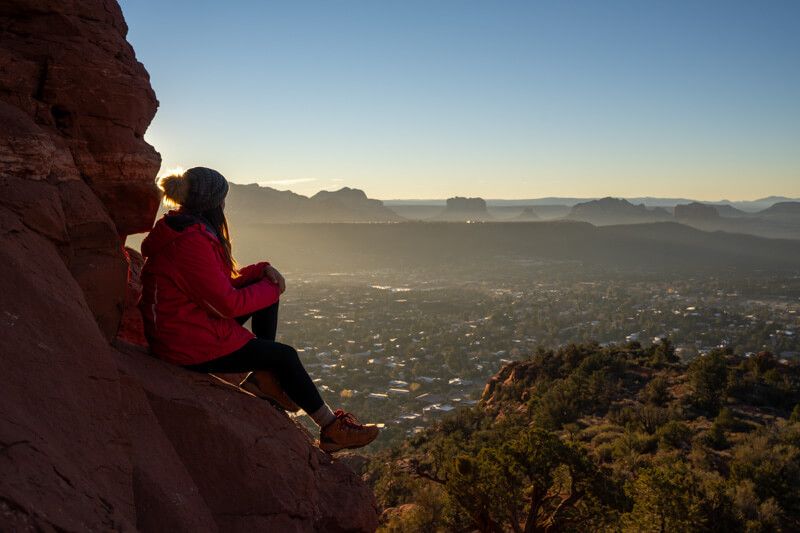Photo of Kristen Morgan sat on rock looking out at Sedona Arizona at sunrise from an elevated vantage point