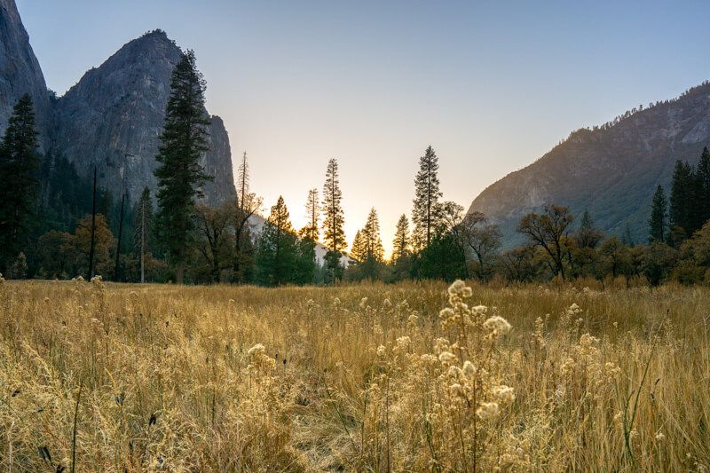 Photo of a wide open valley with golden colored grass leading to a sunset next to granite monoliths