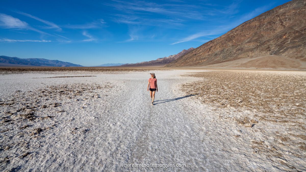 Photo of a tourist walking on salt crystals in a flat wide open landscape in Death Valley National Park